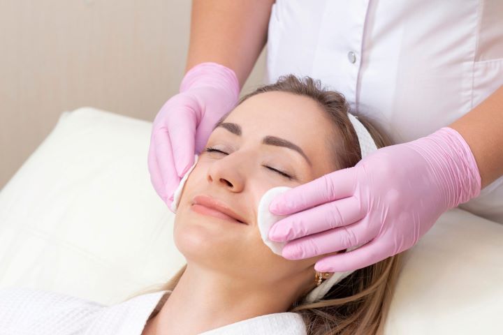 cosmetology lovely young woman with closed eyes receiving facial cleansing procedure beauty salon